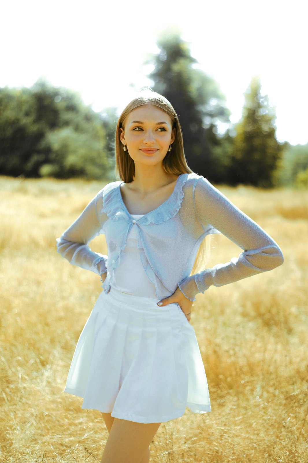 Senior in a sheer blue cardigan, hands on hips in a golden field