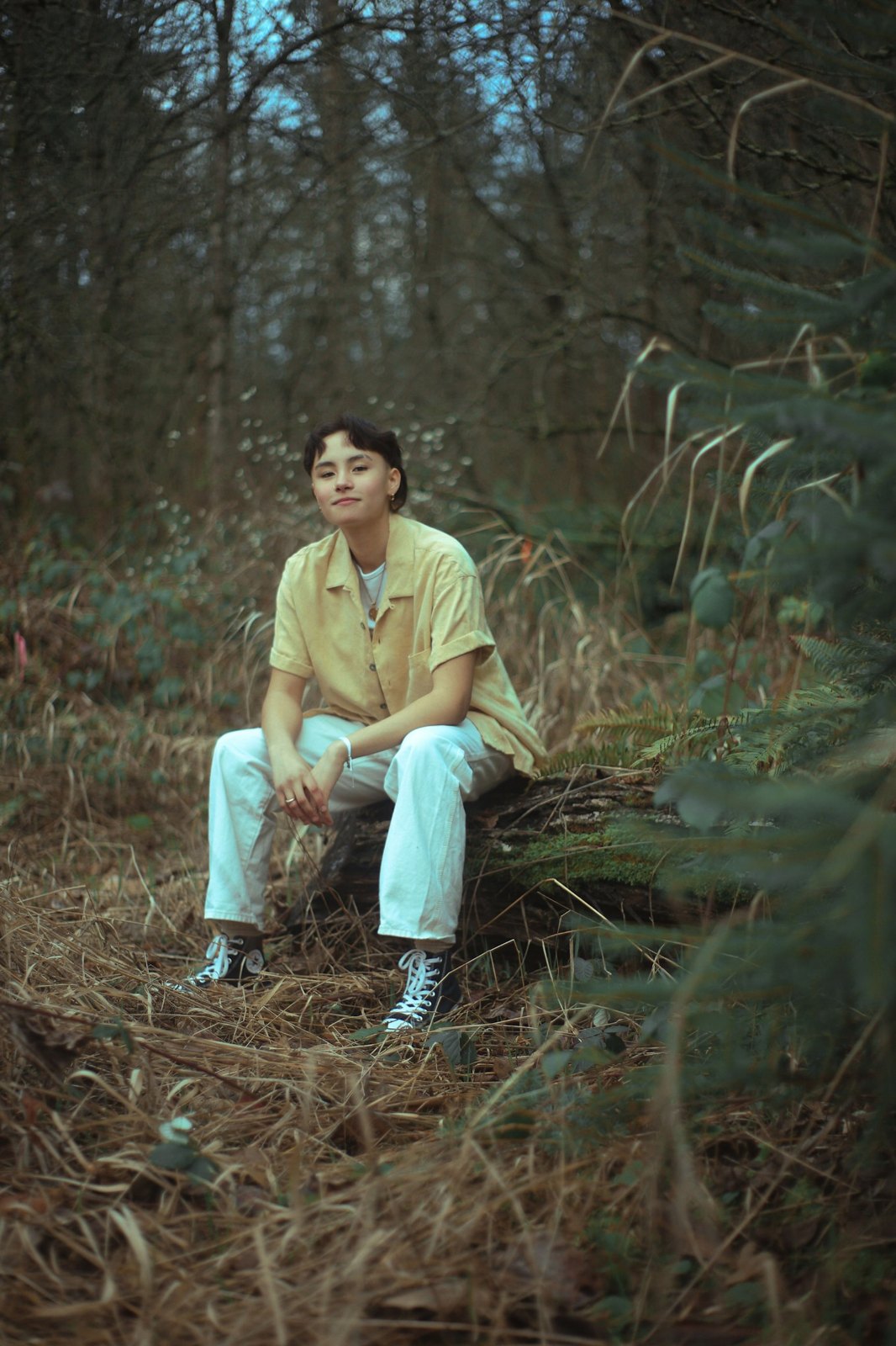 Senior in a yellow shirt seated on a mossy log in the forest