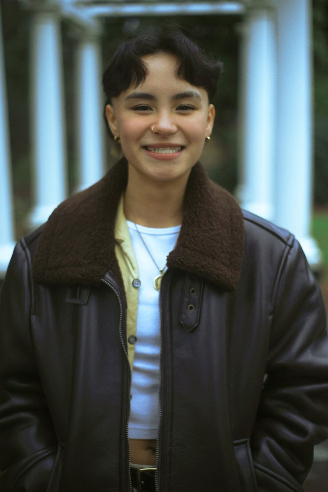 Senior smiling in a leather jacket in front of white columns