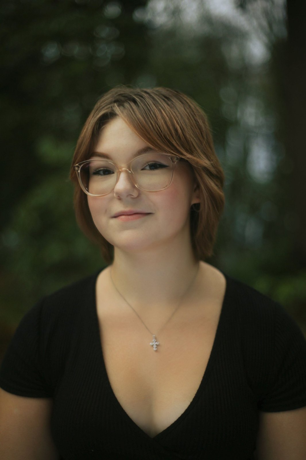 Close portrait of a senior in glasses and a black top among evergreens