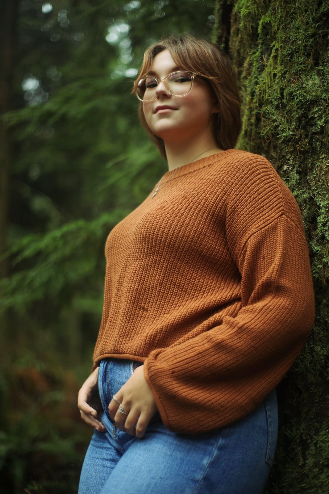 Senior in glasses leaning against a mossy tree