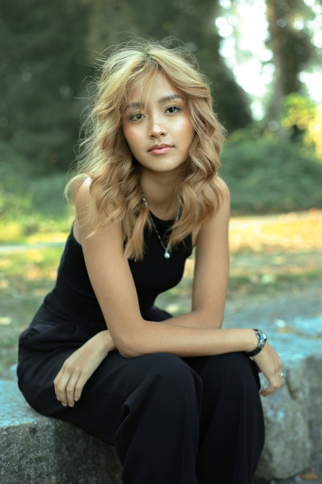 Senior in a black jumpsuit seated on a stone in the park